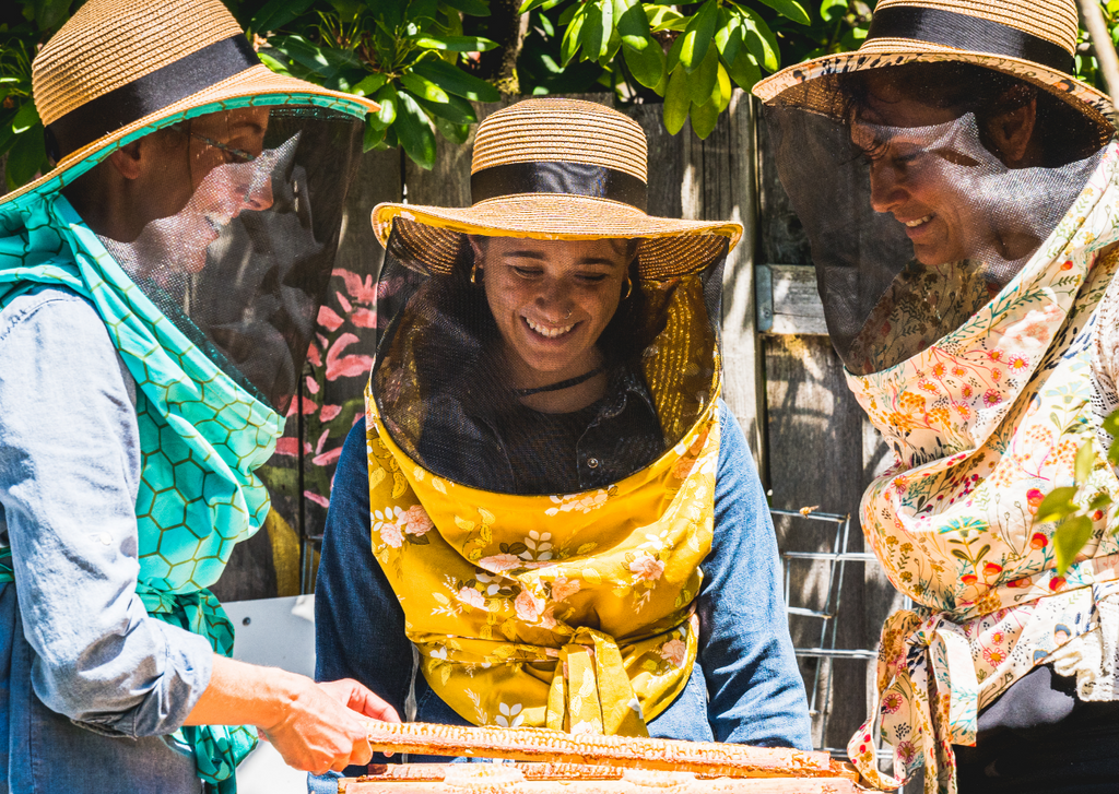 Three people wearing beekeeping suits with visors in a garden setting.