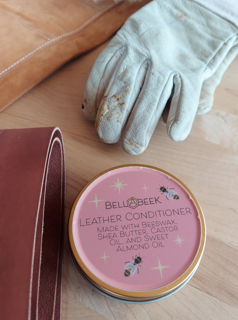 Bella Beek Leather Conditioner made with beeswax, shea butter, castor oil, and sweet almond oil. Leather conditioner tin is arranged with gloves, leather tool rolls.